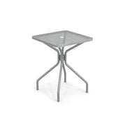 The Cambi Table is a modern, square outdoor indoor table featuring a mesh top with a central hole. Supported by four curved legs that connect in the middle, its gray finish highlights a minimalist, industrial design.