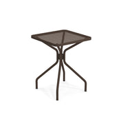 The Cambi Table is a small, square outdoor/indoor table with a brown mesh top. Its four slightly curved legs meet at the center for a sturdy, modern design, while the mesh surface and open frame lend it a lightweight appearance.