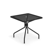 The Cambi Table is a black metal outdoor table featuring a mesh top. Its four curved legs converge at the center and extend outward for added stability. A small circular hole in the middle is perfect for adding an umbrella. Plain white background.