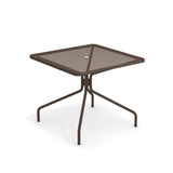 The Cambi Table is a brown metal square table with a mesh top, central umbrella hole, and four slightly curved legs that meet at a central support. Its minimal, modern design makes it perfect for outdoor/indoor use.