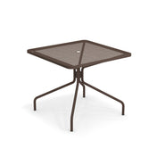 The Cambi Table is a brown metal square table with a mesh top, central umbrella hole, and four slightly curved legs that meet at a central support. Its minimal, modern design makes it perfect for outdoor/indoor use.