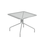 The Cambi Table is a square, light gray outdoor/indoor table with a mesh top, rounded corners, and simple tubular legs that angle outward. A small circular hole in the center allows for an umbrella pole. The design is minimalist and modern.