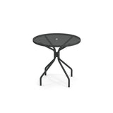 The Cambi Table features a round black metal mesh top with four legs that curve outward and then downward. Designed for outdoor/indoor use, it has a central hole for an umbrella and a simple, modern style against a plain white background.