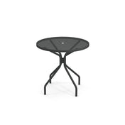 The Cambi Table features a round black metal mesh top with four legs that curve outward and then downward. Designed for outdoor/indoor use, it has a central hole for an umbrella and a simple, modern style against a plain white background.
