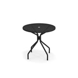 The Cambi Table features a round, black metal frame with a mesh top and a central umbrella hole. Suitable for outdoor/indoor use, its four angled legs and support bars offer sturdy, modern style against a plain white background.