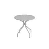 A round, light gray Cambi Table with a mesh top and a central hole, supported by four angled legs connected by a central brace. The simple, modern design makes this outdoor table ideal for patios. The background is plain white.