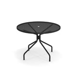The Cambi Table is a round mesh table with four slender, angled legs curving outward to a central support. Its minimalist, modern outdoor table design features a central hole for an umbrella, and it sits elegantly on a white background.