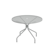 The Cambi Table is a round, gray metal outdoor/indoor table featuring a mesh top and four angled legs converging at the center. Its minimalist, modern design includes a small hole in the middle, perfect for an umbrella. Shown on a plain white background.
