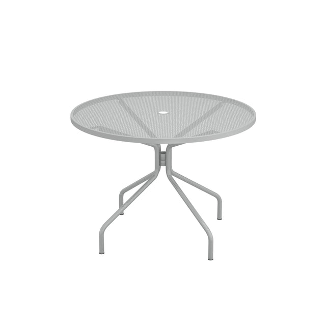 The Cambi Table is a round, gray metal outdoor/indoor table featuring a mesh top and four angled legs converging at the center. Its minimalist, modern design includes a small hole in the middle, perfect for an umbrella. Shown on a plain white background.