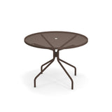 The Cambi Table is a round, metal outdoor table with a mesh top and four angled legs, all in dark brown. It features a small circular hole in the center for an umbrella and is set against a plain white background.