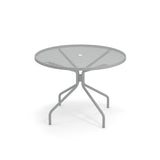 A round outdoor table with a mesh top and a central hole for an umbrella. Its four angled legs curve outward and then downward, ensuring stability on any patio. The background is plain white for a clean, classic look.