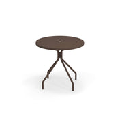A round, dark brown solid steel outdoor table with a central hole on the tabletop, supported by four angled legs that connect to a central vertical post. The table stands on a white background with a faint shadow beneath it.