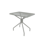 A small, square outdoor/indoor table with a glass top and central hole, supported by a gray metal frame with four angled legs that curve outward. The minimalist, modern Cambi Table blends style and function for any space.
