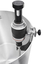Close-up of a KitchenAid Commercial Immersion Blender with a 12 inch stainless steel blending arm, attached to the rim of a large pot. Secured with a clamp and knob, its control dials and display sit atop the metal heating wand submerged in the pot.