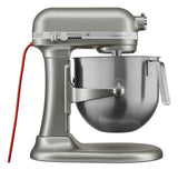 A metallic KitchenAid Commercial Stand Mixer with an 8 quart bowl, a red power cord, and control knobs boasts a classic, industrial design. The mixer features “Commercial” labeling on the side panel for a professional touch.