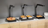 Three buffet-style food warmers with NSF-certified multi-position heat lamps sit on a countertop: sliced pizza, fried chicken and French fries, and bread rolls. Stacks of white plates are on the far right against a gray wall.