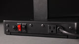 A close-up of the back panel of an NSF-certified electronic device shows two toggle switches—one red and one black—a round connector, a standard electrical outlet, and a power cord plugged in, all mounted on a matte black surface.