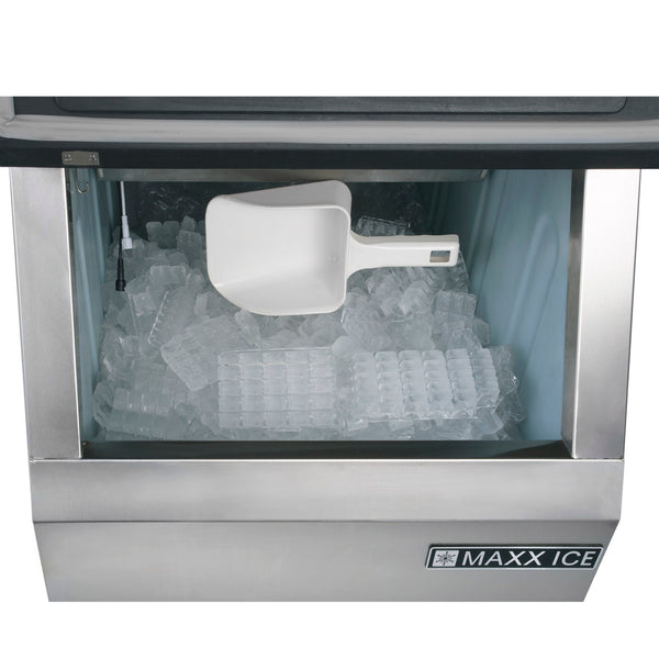 A commercial ice maker filled with clear, rectangular ice cubes sits beneath a white plastic scoop. The stainless steel front features the MAXX ICE logo in the lower right corner, and an ample ice storage bin ensures plenty of supply.