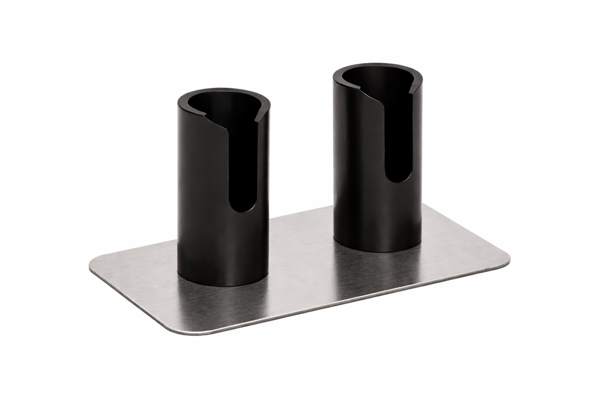 A rectangular metal base supports two upright black cylindrical holders with open side slots. This double Portion Pump Stand by Nemco Food Equipment features evenly spaced holders attached to a flat, brushed metal surface, set against a white background.