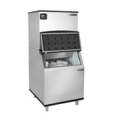 A Maxx Ice commercial stainless steel ice machine with a digital display on top. The upper black door is partly open, revealing ice inside. The lower ice storage bin shows visible ice. This unit, with 580 lbs ice storage, stands on four sturdy legs.