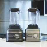 Two silver KitchenAid Commercial Bar Blenders with clear 60 oz pitchers and Patented Talon blades sit side by side on a white kitchen counter, blending seamlessly into a modern kitchen with stainless steel appliances.