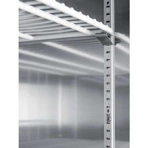 Close-up of a metal refrigerator interior showing adjustable shelf supports, metal rails with regularly spaced slots, and a white wire shelf. The surfaces are clean and reflective, highlighting the industrial, utilitarian design typically found in a commercial refrigerator.