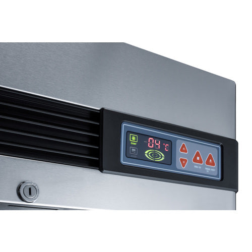 Close-up of a stainless steel commercial refrigerator appliance with a digital control panel displaying 04°C. The panel features several red triangular buttons, a round green icon, a power symbol, and is bordered in black plastic. Part of a vent and a keyhole are also visible.