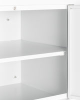 A close-up of an open, empty white wall cabinet with two shelves, viewed from the side. The cabinet door is partially ajar, revealing clean, smooth surfaces and metal mounting hardware securing the adjustable shelves in place. The background is plain and out of focus.