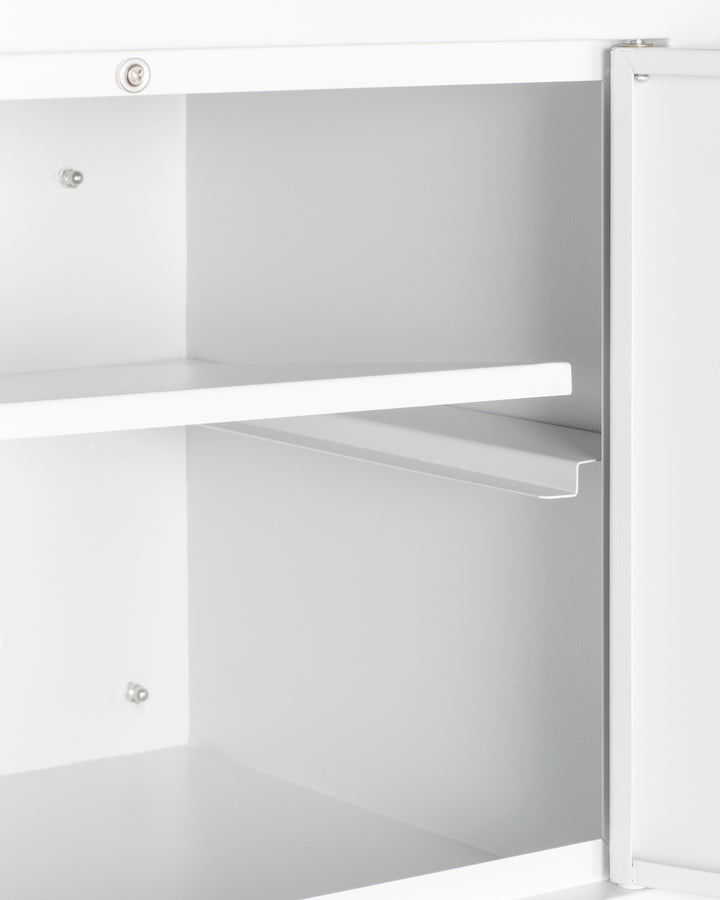 A close-up of an open white metal wall cabinet with two adjustable shelves and a partially open door on the right side, revealing the empty clean interior and visible silver mounting hardware and screws on the sides.