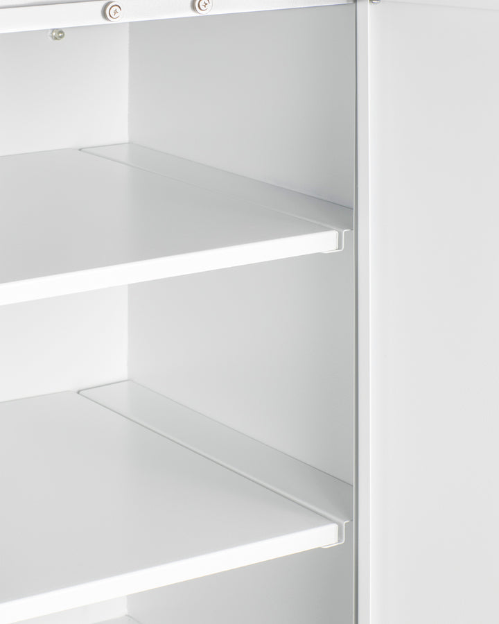 Close-up of a white metal shelving unit with two adjustable shelves, viewed from an angle. Ideal for kitchenettes or as a wall cabinet, the shelves are empty, and the edges and brackets are visible, highlighting the clean, minimal design. The lighting is bright, showing smooth surfaces.