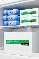 Inside an Accucold medical freezer, three blue ice packs are on the top shelf, next to two white boxes labeled Varicella Virus Vaccine Live VARIVAX Store Frozen. A larger box with the same label is on the bottom, against a white interior background. This compact all-freezer features NIST calibrated temperature monitoring for reliable vaccine storage.