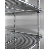 Close-up of empty metal wire shelves mounted inside a stainless steel cabinet or blanket warmer. The adjustable shelves are supported by vertical metal slotted rails attached to the back wall. The scene is well-lit, highlighting the clean, reflective surfaces.