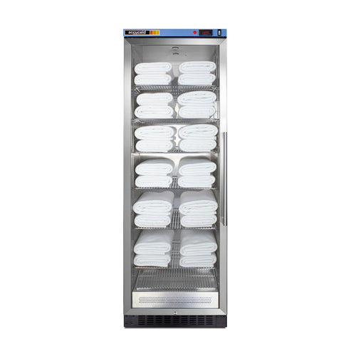 A tall, glass-fronted blanket warmer with a stainless steel frame holds neatly folded white towels on multiple adjustable wire shelves, arranged in rows from top to bottom. The machine features a digital control panel on top and a vented section at the bottom, utilizing passive heating technology to maintain optimal warmth.