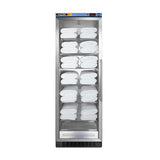 A tall, glass-fronted blanket warmer with a stainless steel frame holds neatly folded white towels on multiple adjustable wire shelves, arranged in rows from top to bottom. The machine features a digital control panel on top and a vented section at the bottom, utilizing passive heating technology to maintain optimal warmth.