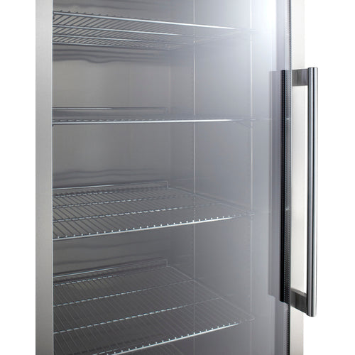 A close-up of a stainless steel refrigerator with a see-through glass door, featuring adjustable shelves inside. The interior shows empty wire shelves and a tall vertical handle on the right side of the door. The surfaces are clean and shiny, reflecting light.