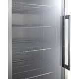 A close-up of a stainless steel refrigerator with a see-through glass door, featuring adjustable shelves inside. The interior shows empty wire shelves and a tall vertical handle on the right side of the door. The surfaces are clean and shiny, reflecting light.
