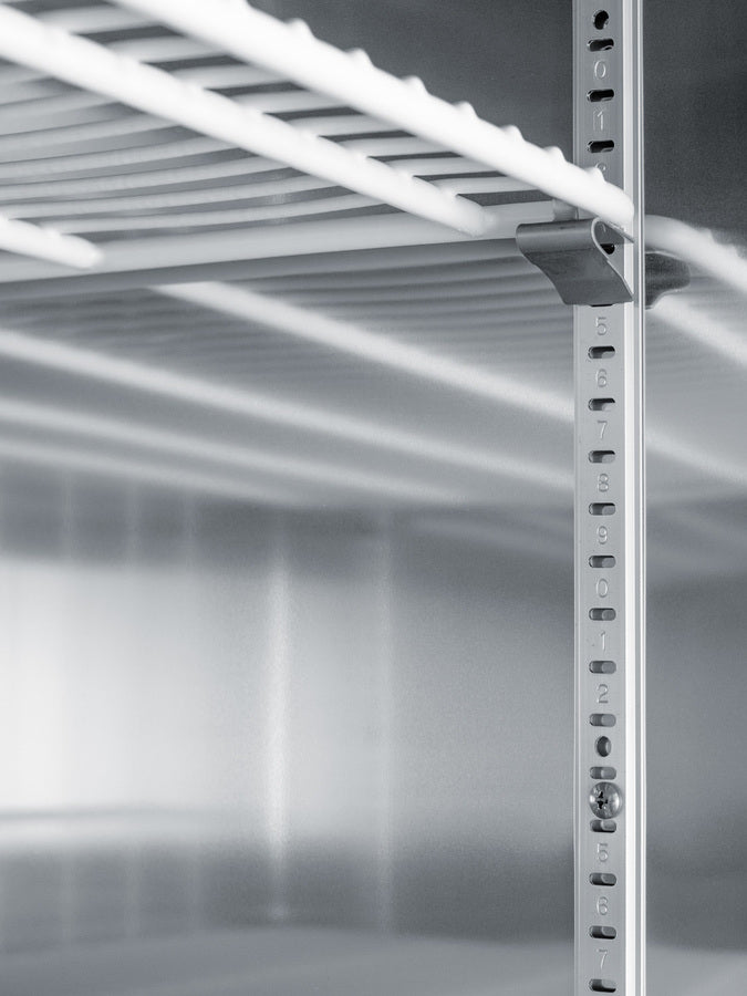 Close-up of a metal shelving unit inside an empty stainless steel freezer. The vertical support features numbered holes for adjustable shelving, typical of commercial upright freezers. The horizontal shelf bars create strong lines and cast soft shadows, contributing to a modern, industrial look.
