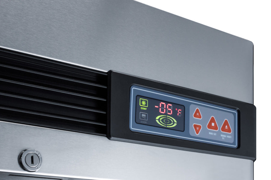 Close-up of a commercial upright freezer’s stainless steel control panel displaying -05°F in green digits, with several red triangular buttons and a circular green icon. The panel is bordered in black; vent slats and a lock are visible on the left side.