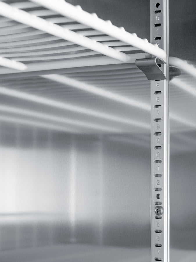 Close-up of a metal shelving unit corner, showing a numbered vertical support post with adjustable shelf slots. The parallel white shelves cast shadows on the metallic background, reminiscent of those found inside a commercial refrigerator. The environment is clean and minimalistic, suggesting industrial or storage use.