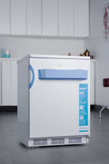 An Accucold Medical Freezer stands in a modern, clean clinical room with white cabinets, grey flooring, and medical supplies on counters in the background. This white undercounter all-freezer features a blue handle and information label, and its ADA compliant design makes it ideal for accessible medical storage.