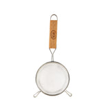 A round metal mesh strainer with a fine mesh sieve, featuring a wooden handle engraved with text. The handle has a metal loop for hanging, and the strainer has two support hooks at the base for stable use over a bowl.