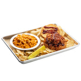 A 1/4 size aluminum sheet pan holds a pulled pork sandwich with barbecue sauce on a sesame bun, potato chips, macaroni and cheese in a white bowl, and a sliced dill pickle spear. The background is plain white.