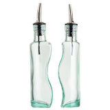 Two clear glass bottles with curvy, wavy sides are shown upright. Each features a stainless steel pourer with a black rubber stopper. The bottles are empty, positioned side by side against a white background. They are also dishwasher safe.