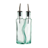 Two clear glass oil and vinegar bottles are fused together side by side, each with stainless steel pourers and black rubber stoppers. The slightly wavy glass bottles are empty, standing upright against a white background.