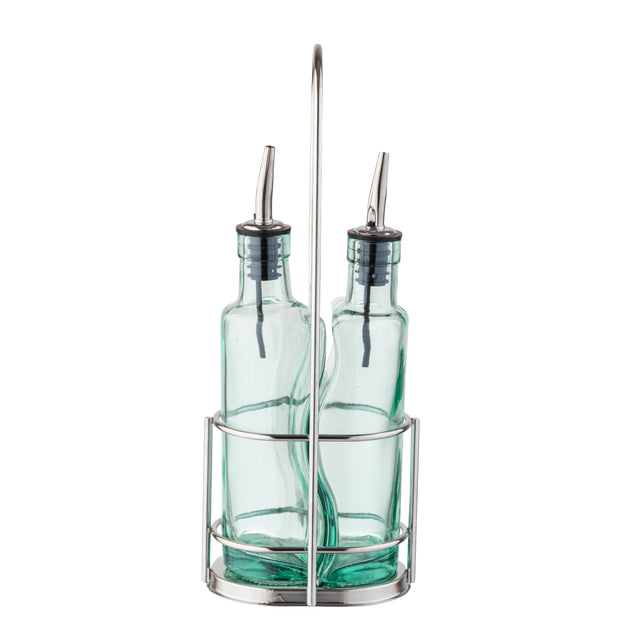 Two green tinted glass bottles with stainless steel pourers sit side by side in a silver metal caddy with a tall handle. The bottles appear empty and are likely intended for olive oil or vinegar. The design is simple and modern.