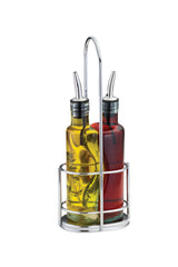 The Gemelli bottle set features green tinted glass bottles with stainless steel pourers in a chrome caddy. One holds yellow olive oil with herbs, the other red vinegar. The caddy has a handle for easy carrying and a round base that keeps bottles upright.
