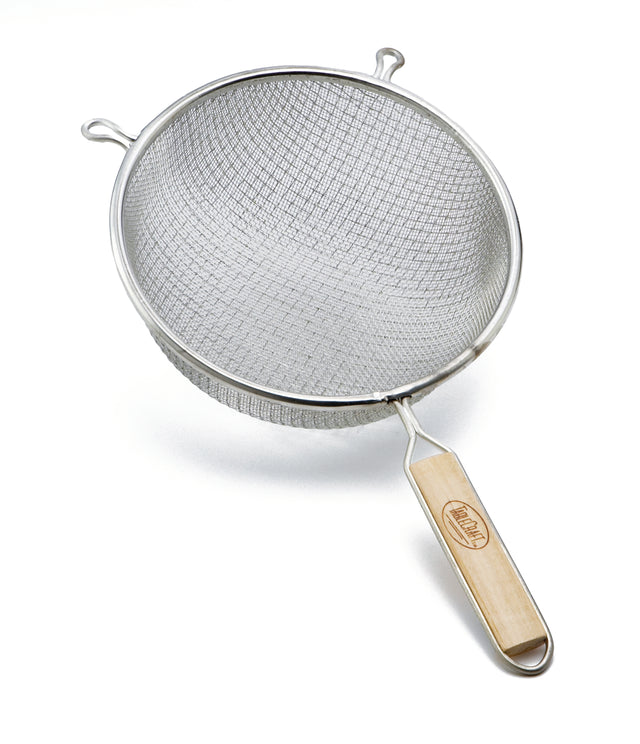A metal strainer with a double medium mesh and round bowl is shown. It features two small side hooks and a long wooden handle with a brand name, making it ideal for sifting or draining food. The strainer rests on a white background.
