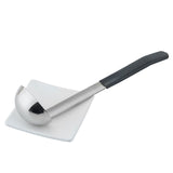 A stainless steel, dishwasher safe soup ladle with a black handle rests diagonally across a small, square white plate. The ladle’s bowl is deep and shiny, reflecting light, and the plate sits on a plain white background.