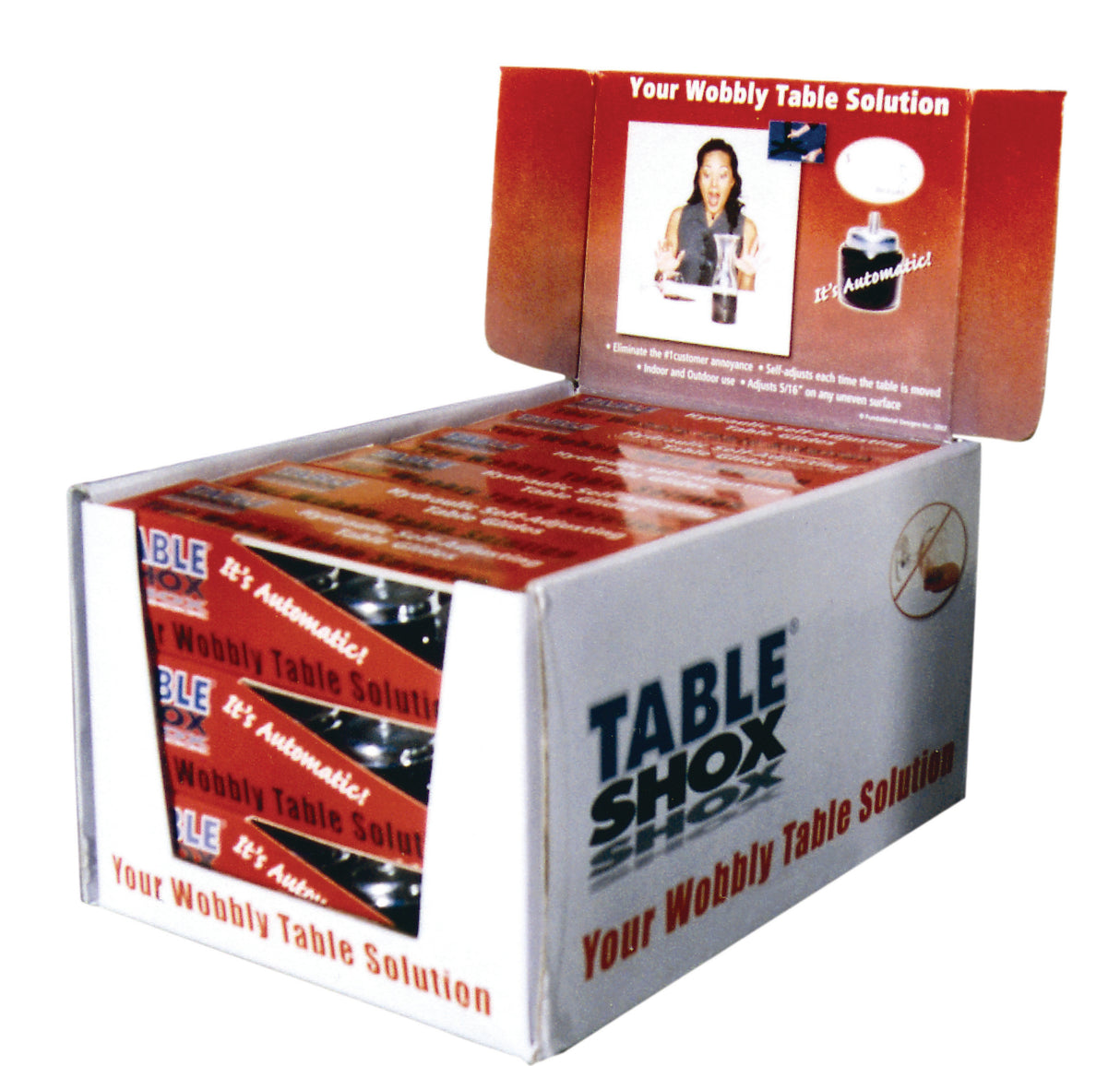 Open display box of TABLE SHOX products, labeled Your Wobbly Table Solution. The box shows several red-packaged Table Shox Glide furniture levelers inside, and the lid features a woman by a table plus product instructions. Branding and slogans are clearly visible.