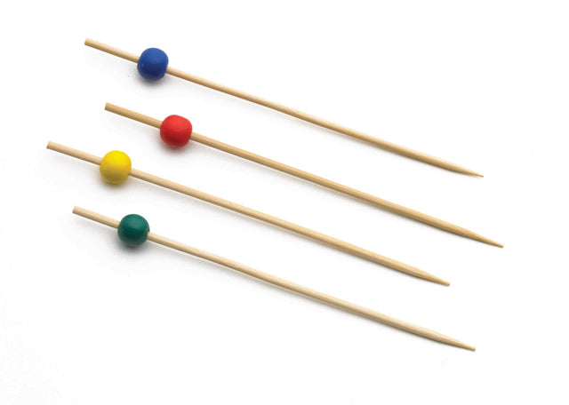 Four TableCraft Products bamboo picks are arranged diagonally on a white background, each featuring a single bead in assorted colors—blue, red, yellow, and green—near the pointed tip. The colorful beads are evenly spaced on the skewers.